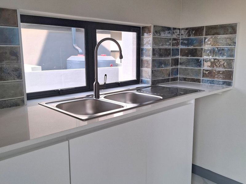 A modern, clean kitchen area featuring a stainless steel double sink, quartz countertops, and stylish subway tile splashbacks with marble-look floor tiles.