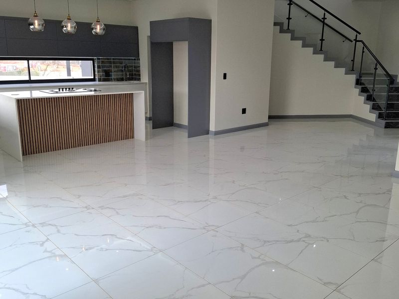Modern open-plan living area featuring a sleek kitchen island, high-end marble-look floor tiles, and a contemporary staircase with a glass balustrade.
