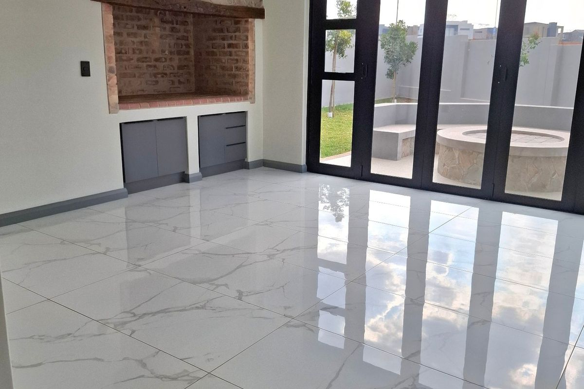 Spacious living area featuring polished marble-look floor tiles, a built-in brick fireplace with stone detailing, and large bi-fold doors opening to an outdoor patio.