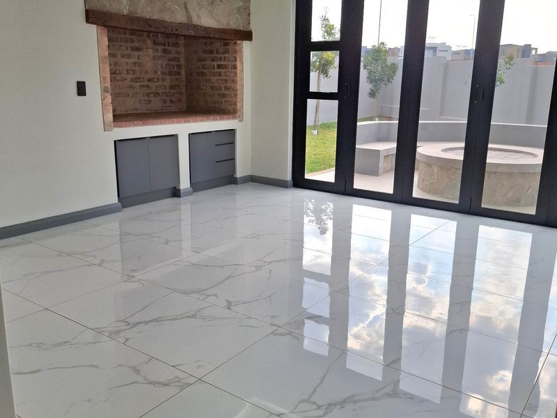 Spacious living area featuring polished marble-look floor tiles, a built-in brick fireplace with stone detailing, and large bi-fold doors opening to an outdoor patio.