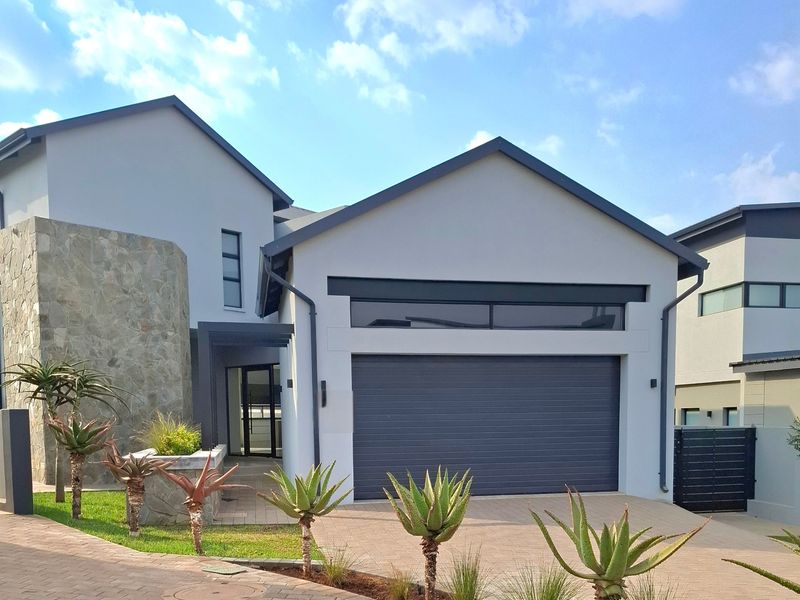 Modern front elevation featuring stone cladding, a paved driveway, and a sleek sectional garage door with a transom window.
