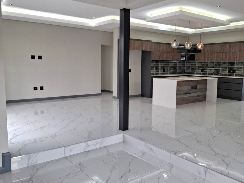 Spacious open-plan living and kitchen area featuring modern marble-look floor tiles, recessed ceiling lighting, and a contemporary kitchen island with built-in cabinetry.