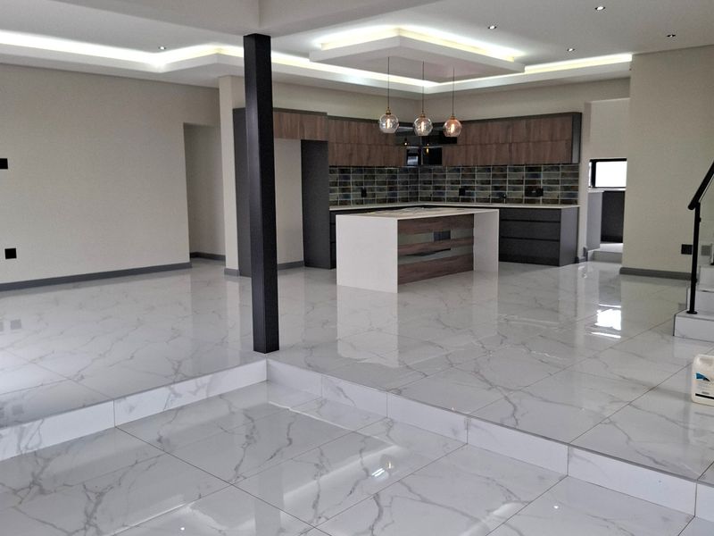 Spacious open-plan living and kitchen area featuring modern cabinetry, a central island, recessed ceiling lighting, and polished marble-look floor tiles on a raised platform.