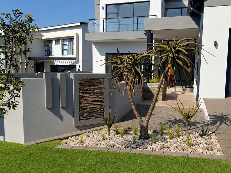 Modern double-story residential facade featuring clean architectural lines, stone cladding accents, a glass balcony, and a well-maintained landscaped front garden.