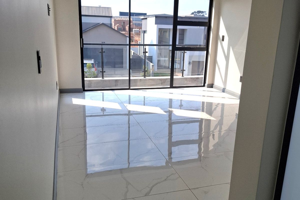 A bright, modern, and empty living area featuring polished porcelain floor tiles, recessed lighting, and a large sliding door leading to a balcony.