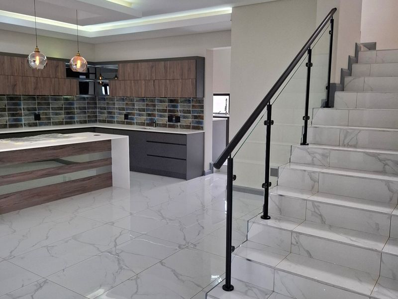 Modern open-plan kitchen featuring a central island, sleek cabinetry, and a striking tiled staircase with a contemporary glass balustrade.