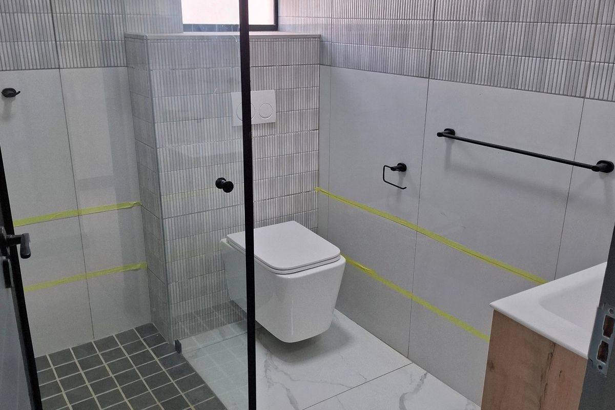 Modern bathroom featuring a wall-hung toilet, glass shower enclosure, and vanity cabinet, currently in the final stages of completion.