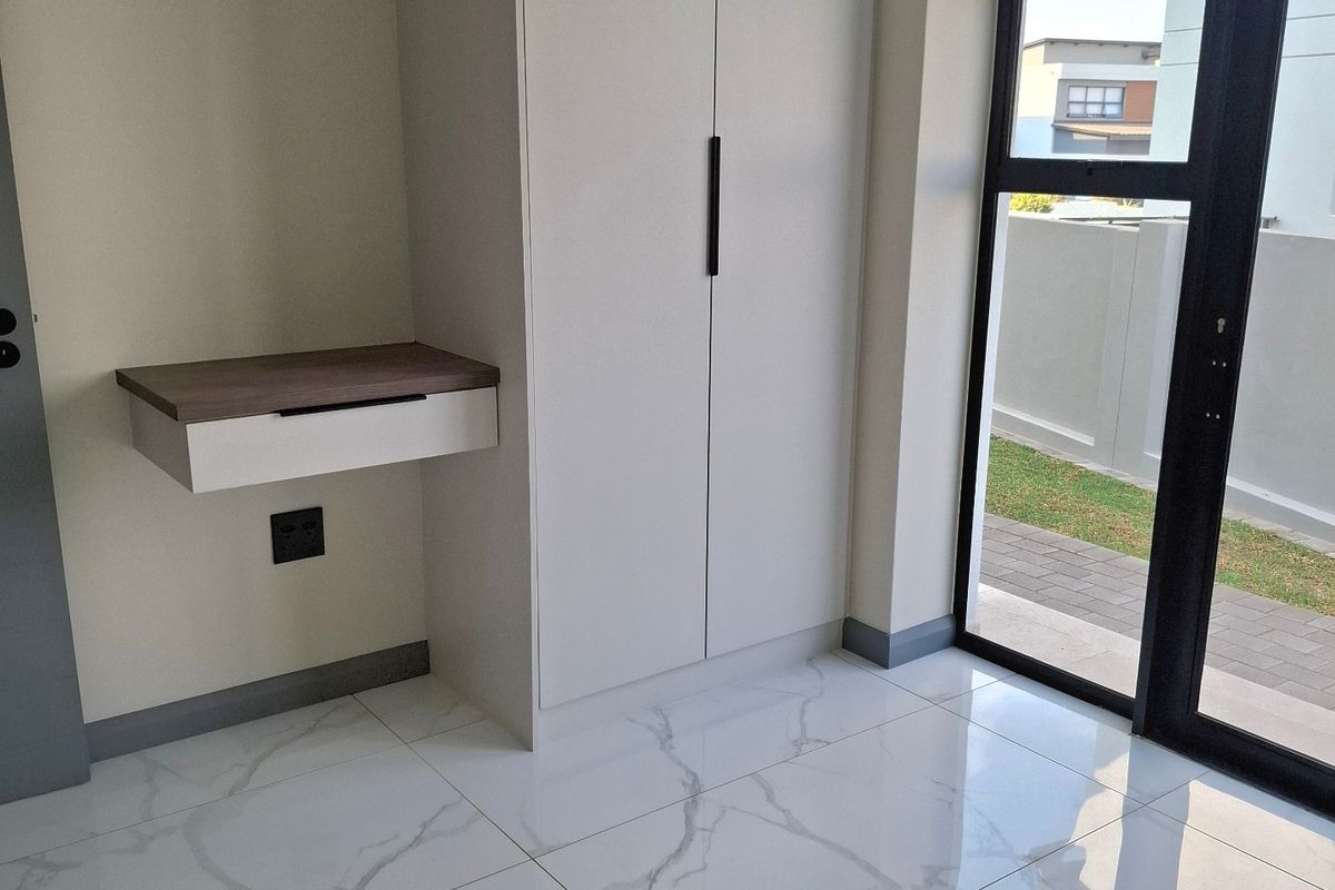 Modern bedroom featuring high-gloss marble-look floor tiles, a built-in wardrobe, a floating vanity unit, and direct access to the outdoor area via a glass door.