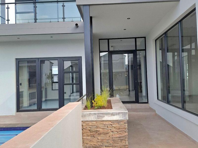 Modern covered patio area featuring tiled flooring, a stone-clad planter, and large glass doors leading into the home, adjacent to a swimming pool.