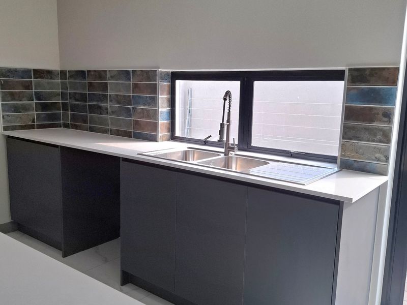 A modern, clean scullery featuring dark grey cabinetry, white quartz countertops, a double stainless steel sink, and stylish subway tile splashbacks.