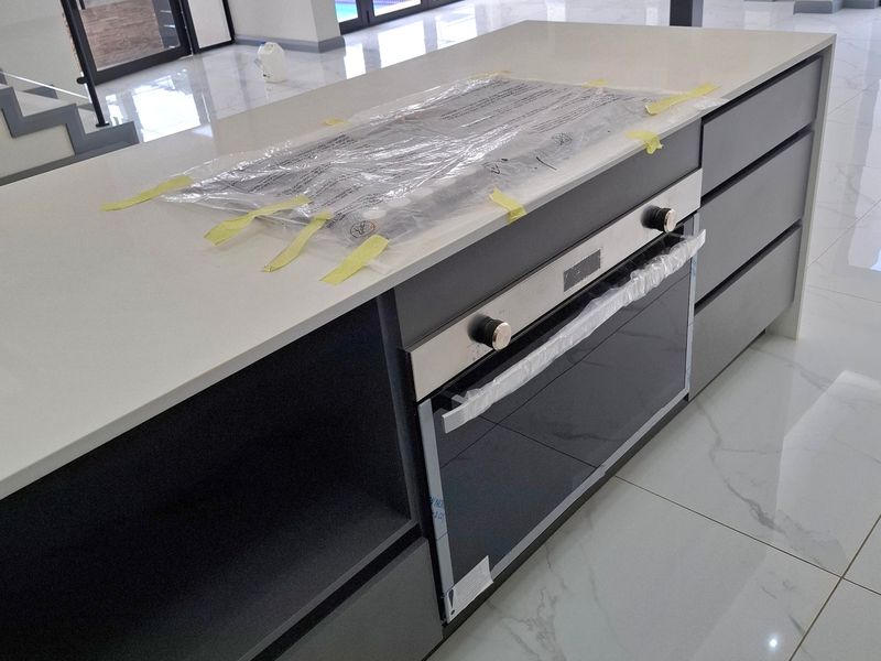 Modern kitchen island featuring a built-in oven, stone countertop, and sleek cabinetry, set against a backdrop of large sliding glass doors and polished floor tiles.
