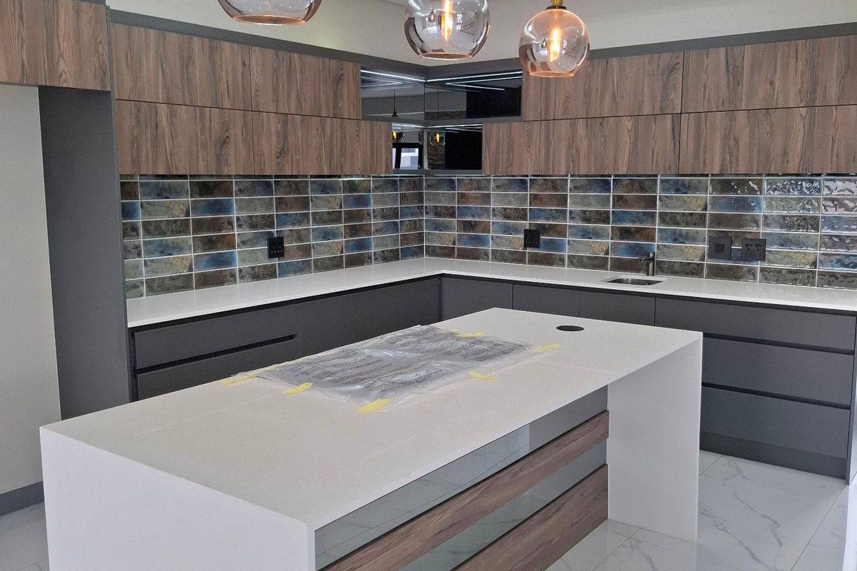 Modern kitchen featuring a large central island with quartz countertops, wood-grain cabinetry, decorative subway tile backsplash, and contemporary pendant lighting.