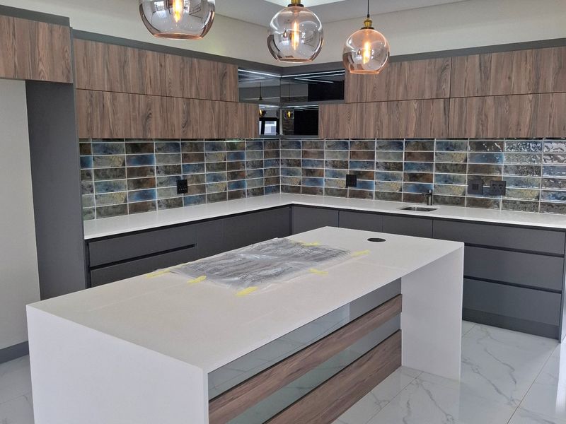 Modern kitchen featuring a large central island with quartz countertops, wood-grain cabinetry, decorative subway tile backsplash, and contemporary pendant lighting.