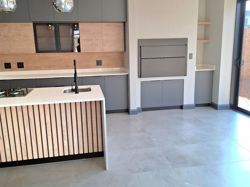 Modern kitchen featuring a central island with stone countertops, built-in cabinetry, and an integrated indoor braai area with sleek grey and wood finishes.