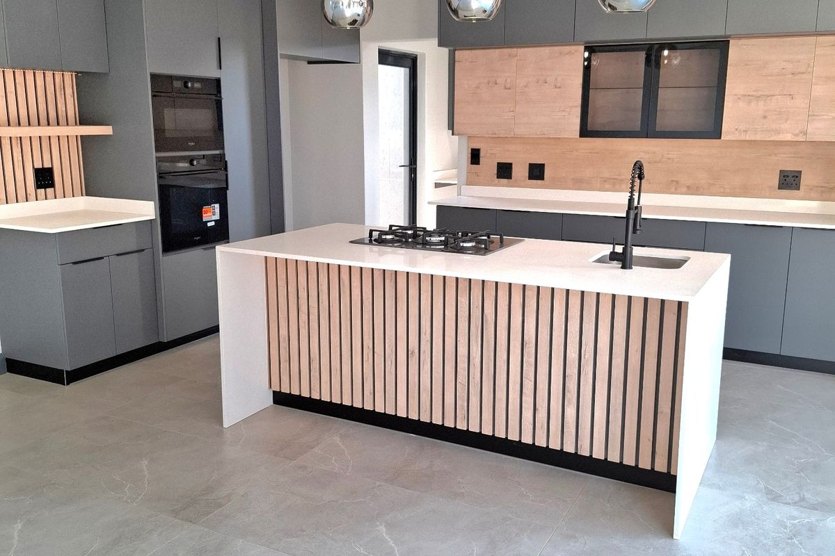Modern, high-end kitchen featuring a central island with gas hob, integrated appliances, custom cabinetry, and stylish drop ceiling with pendant lighting.