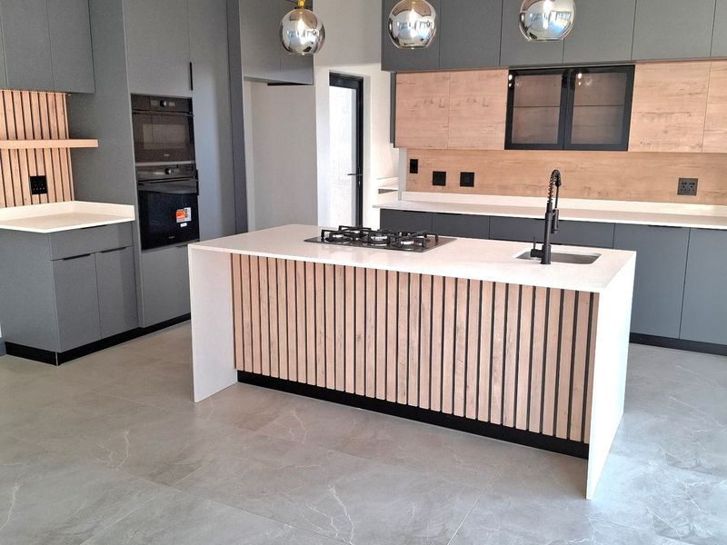 Modern, high-end kitchen featuring a central island with gas hob, integrated appliances, custom cabinetry, and stylish drop ceiling with pendant lighting.