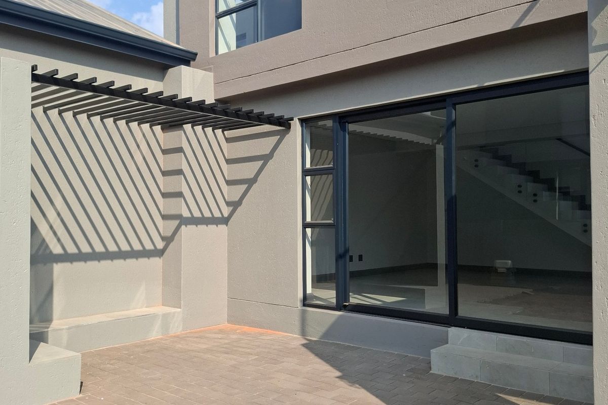 Modern rear exterior featuring a paved patio area, pergola, and large sliding glass doors leading into the home's interior.
