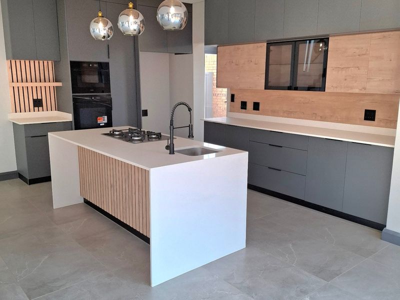 Modern, newly renovated kitchen featuring a central island with gas hob, sleek grey and wood-tone cabinetry, stone countertops, and a decorative slatted ceiling feature.
