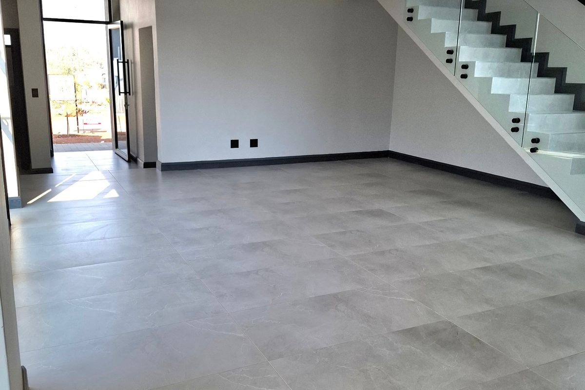 Spacious, modern open-plan living area featuring large-format porcelain floor tiles, recessed lighting, and a contemporary staircase with a glass balustrade.