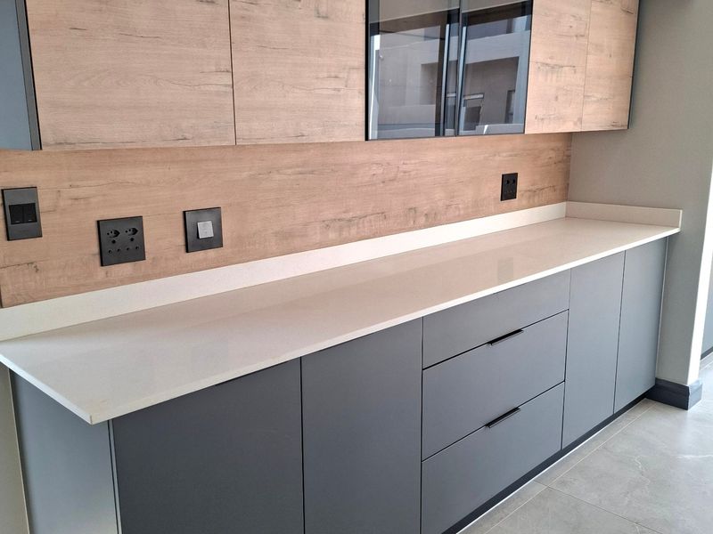 Modern kitchen featuring sleek grey cabinetry, wood-look splashback, stone countertops, and high-quality tiled flooring in a clean, contemporary design.