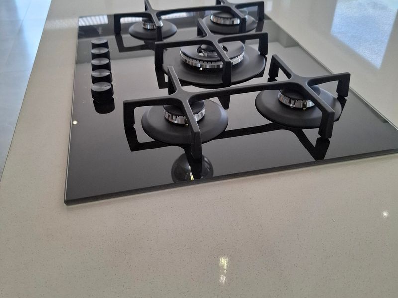 Modern kitchen island featuring a sleek black gas cooktop, stone countertop, and an undermount sink with a contemporary gooseneck faucet.