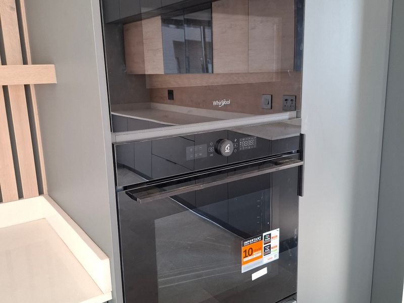 Modern kitchen featuring a sleek, integrated Whirlpool oven and microwave stack with contemporary grey cabinetry and a clean quartz countertop.