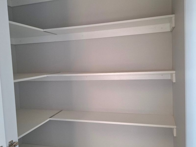 A clean, empty walk-in pantry or storage cupboard featuring multiple levels of white built-in shelving.