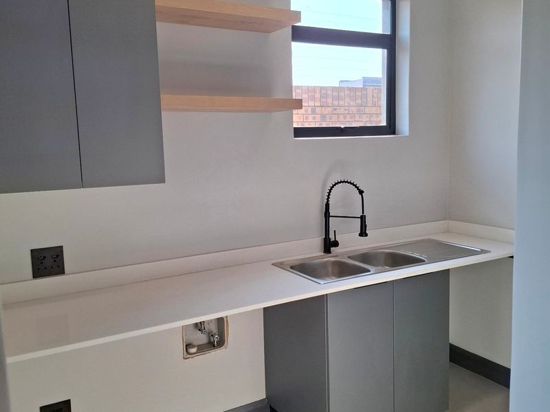 Modern laundry room featuring sleek grey cabinetry, stone countertops, a double basin sink with a gooseneck faucet, and floating timber shelves.