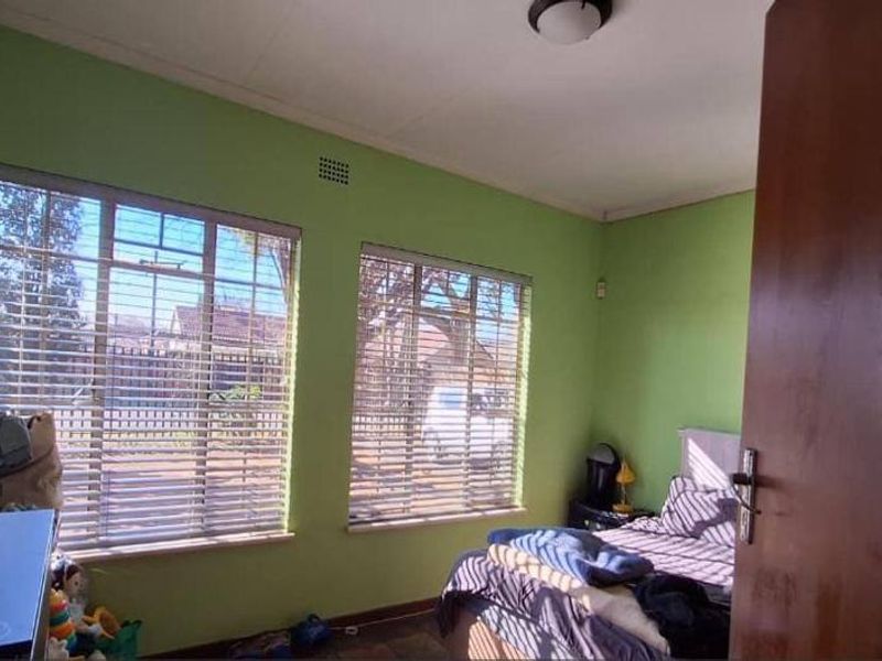 A bedroom featuring steel-framed windows with security bars and a simple ceiling light fixture.