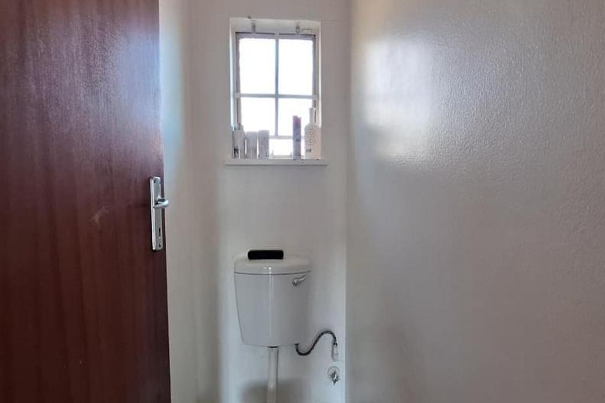 A compact, functional bathroom featuring a standard toilet and a small window, providing essential utility in a simple, clean layout.