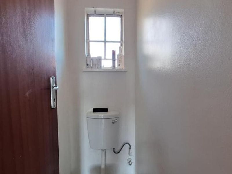 A compact, functional bathroom featuring a standard toilet and a small window, providing essential utility in a simple, clean layout.