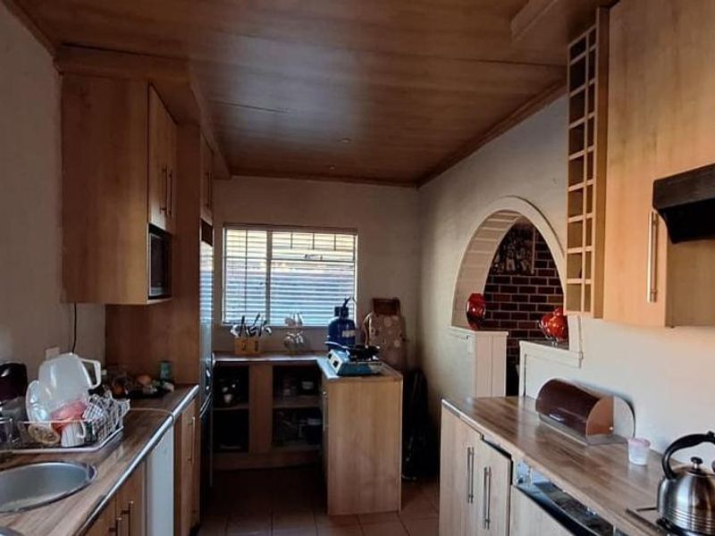A functional kitchen featuring wooden cabinetry, laminate countertops, and an integrated extractor fan, connected to an adjacent space via a decorative archway.