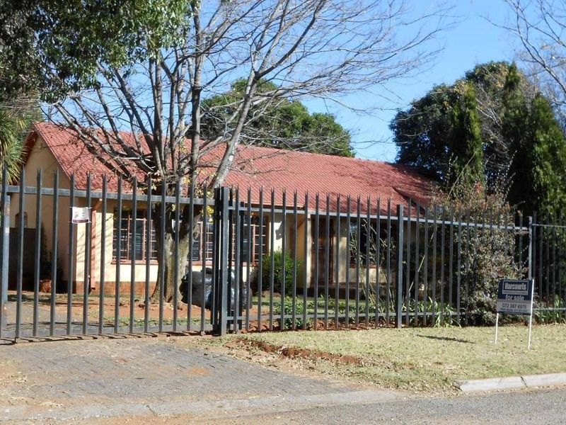 Front view of a single-story residential house featuring a tiled roof, brick exterior, and secure metal perimeter fencing with a paved driveway.
