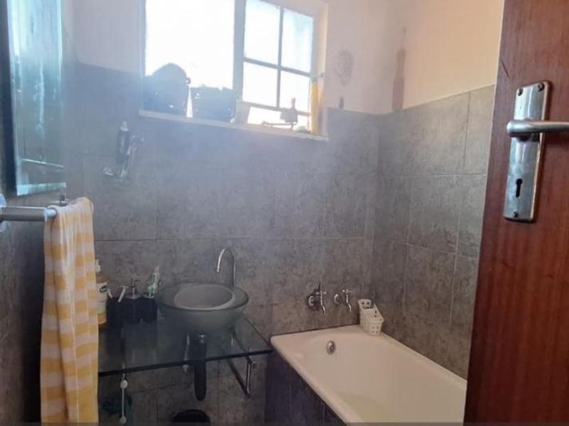 A compact bathroom featuring a glass vessel sink, built-in bathtub, and full-height wall tiling.