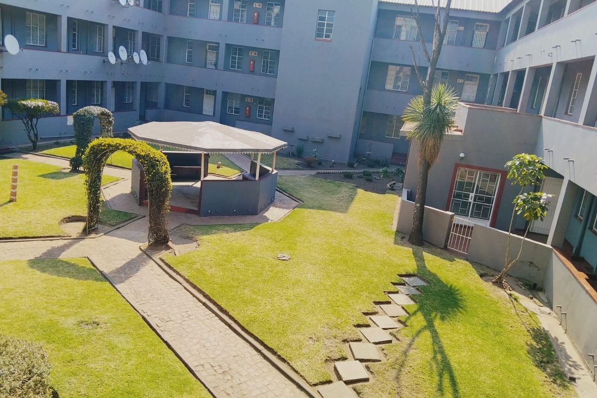 An elevated view of a communal apartment complex courtyard featuring a well-maintained lawn, paved pathways, and a central gazebo structure.