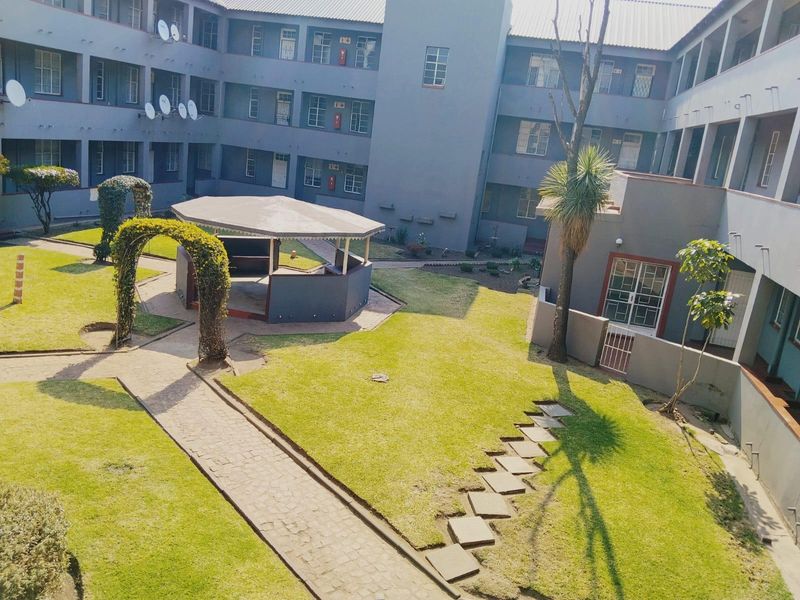 An elevated view of a communal apartment complex courtyard featuring a well-maintained lawn, paved pathways, and a central gazebo structure.