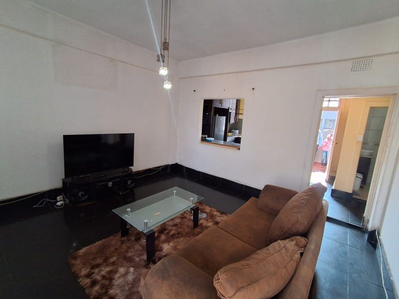 A living room featuring dark floor tiles, a pass-through window connecting to the kitchen, and modern pendant lighting.