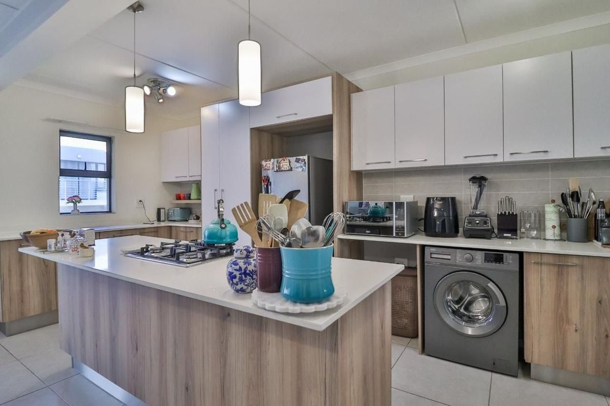 Modern kitchen featuring light wood-tone cabinetry, stone countertops, a central island with a gas hob, and integrated laundry facilities.