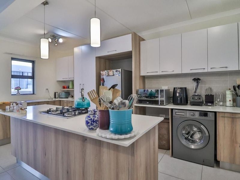 Modern kitchen featuring light wood-tone cabinetry, stone countertops, a central island with a gas hob, and integrated laundry facilities.