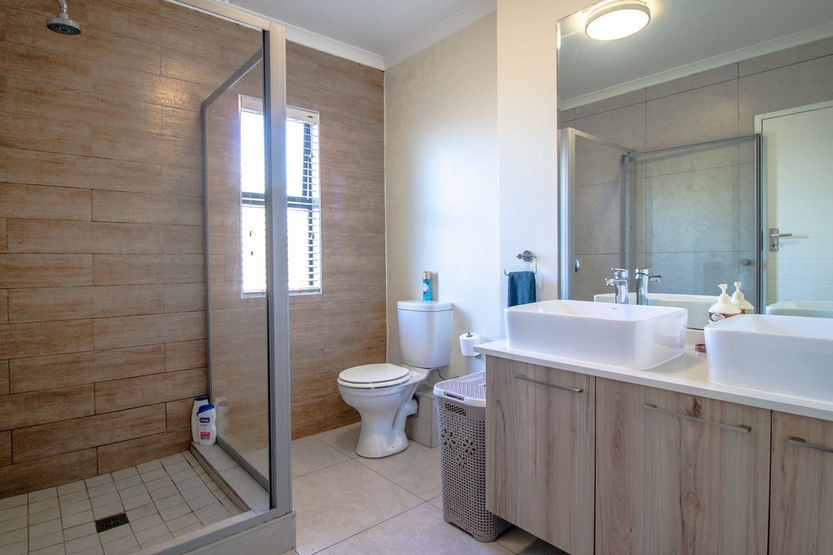 Modern bathroom featuring a walk-in shower with wood-look tile, dual vessel sinks on a wood-finish vanity, and a large wall mirror.