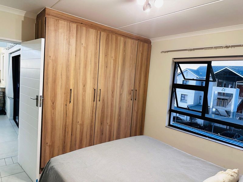 A well-maintained bedroom featuring floor-to-ceiling wood-finish built-in cupboards and a modern aluminium-framed window.