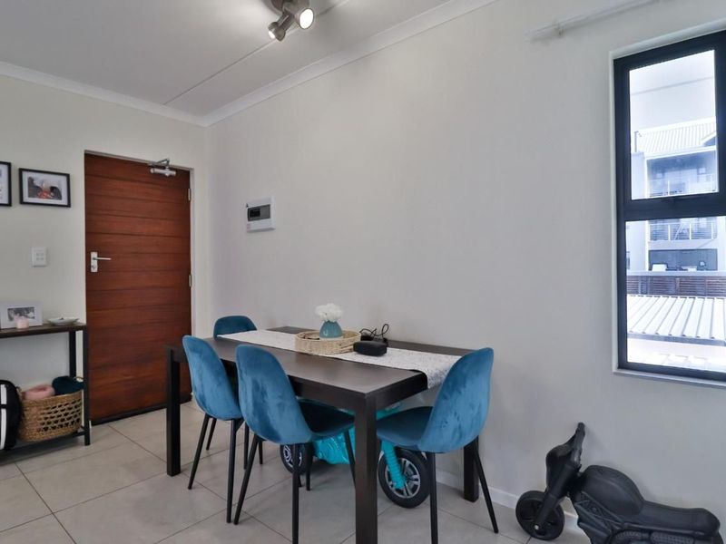 A bright dining area featuring neutral tiled flooring, modern aluminium window frames, and a solid timber door, providing a clean and functional space.