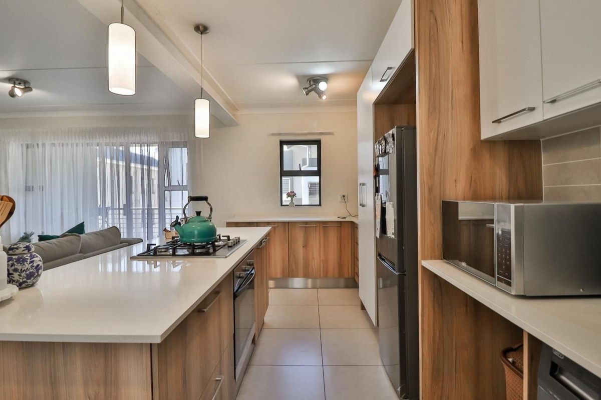 Modern open-plan kitchen featuring a central island with gas hob, stone countertops, and sleek wood-finish cabinetry, seamlessly flowing into the living area.