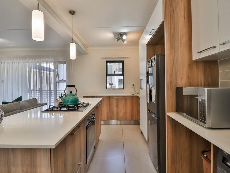 Modern open-plan kitchen featuring a central island with gas hob, stone countertops, and sleek wood-finish cabinetry, seamlessly flowing into the living area.