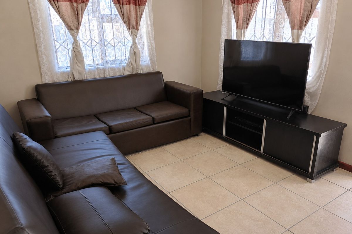 A living room featuring tiled flooring and windows fitted with security bars.