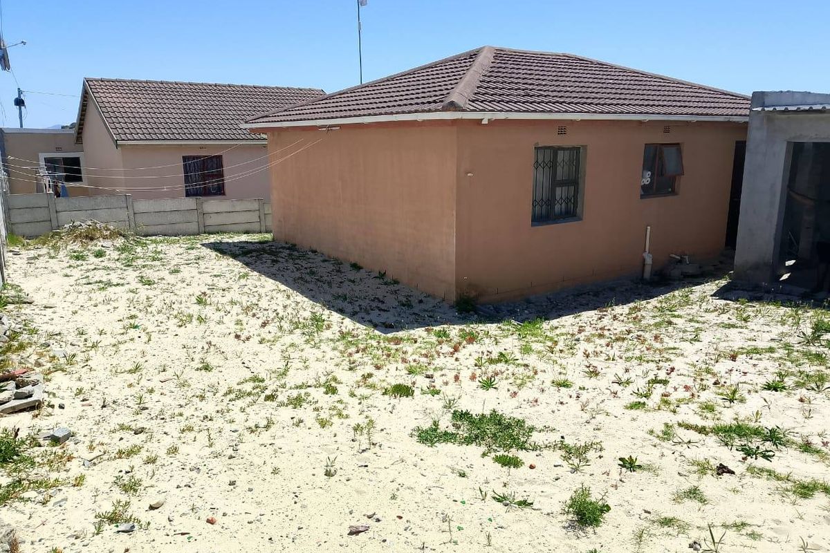 Rear view of the property showing the exterior facade, tiled roof, security bars on windows, and an unlandscaped sandy backyard area.