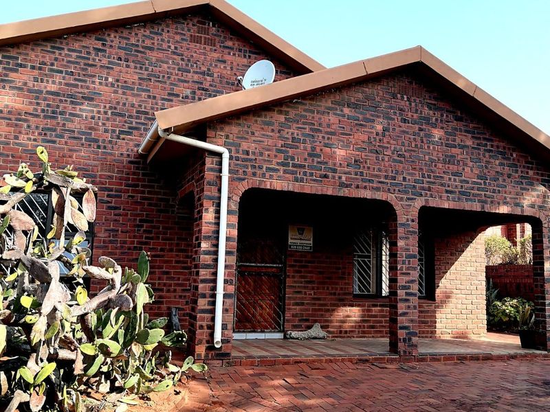 A well-maintained face brick house featuring a covered front porch, paved driveway, and secure entrance with a security gate.
