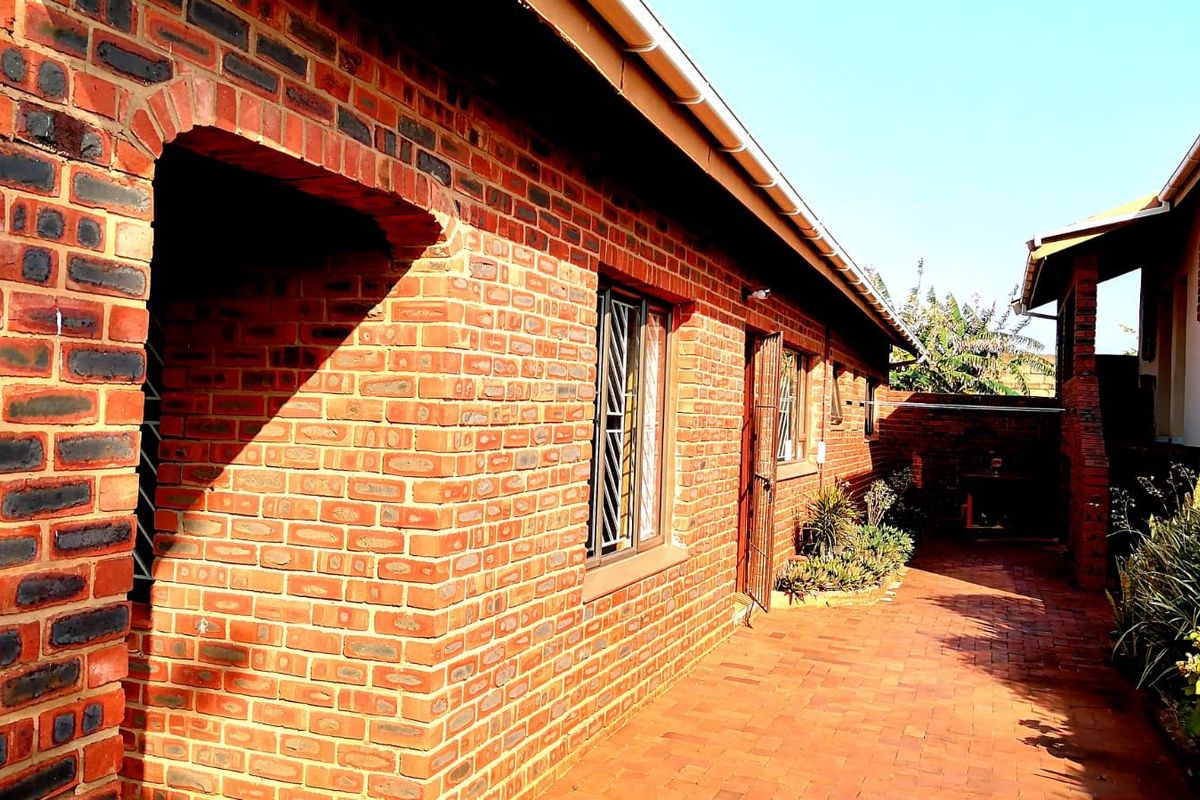 A well-maintained rear exterior view featuring classic face brick construction, a paved patio area, and secure window treatments.