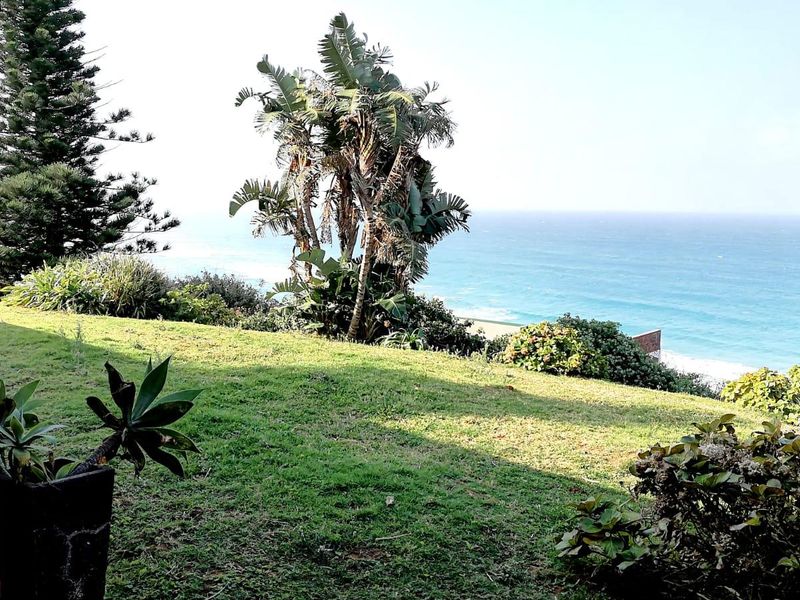 A scenic view of the ocean from a landscaped garden, featuring a rustic brick pillar in the foreground.