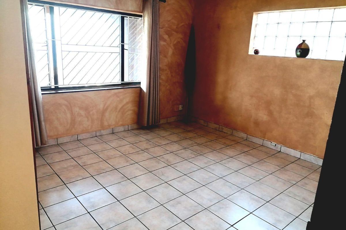 An empty bedroom featuring tiled flooring, textured walls, and a combination of a standard window with security bars and a glass block window.